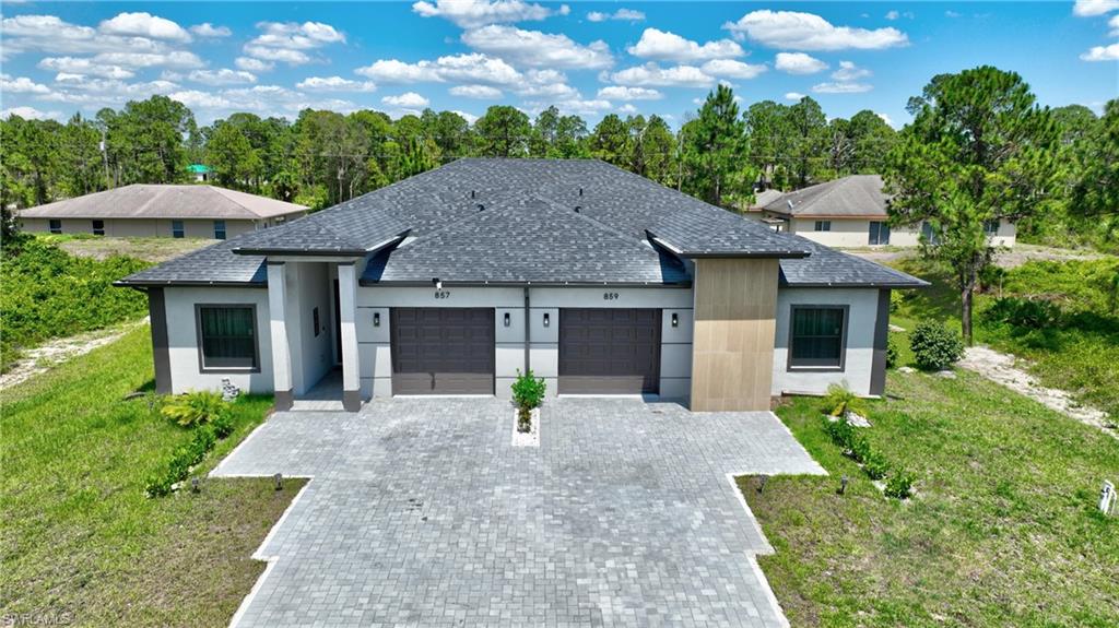 View of front of property featuring an attached garage, decorative driveway, a shingled roof, stucco siding, and a front lawn