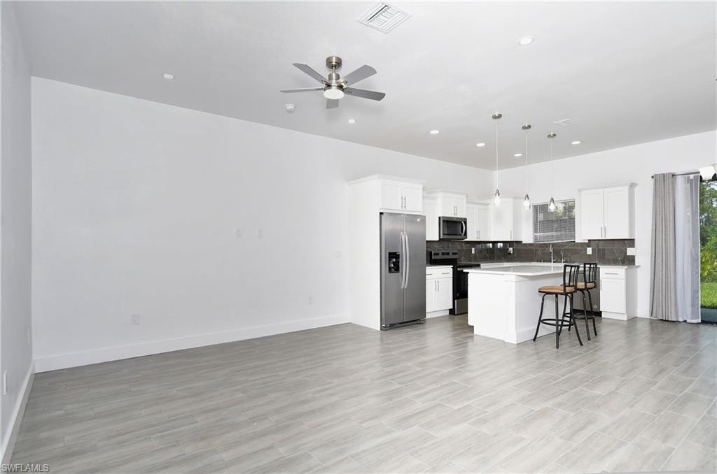 Kitchen featuring stainless steel appliances, open floor plan, hanging light fixtures, a breakfast bar, and a kitchen island