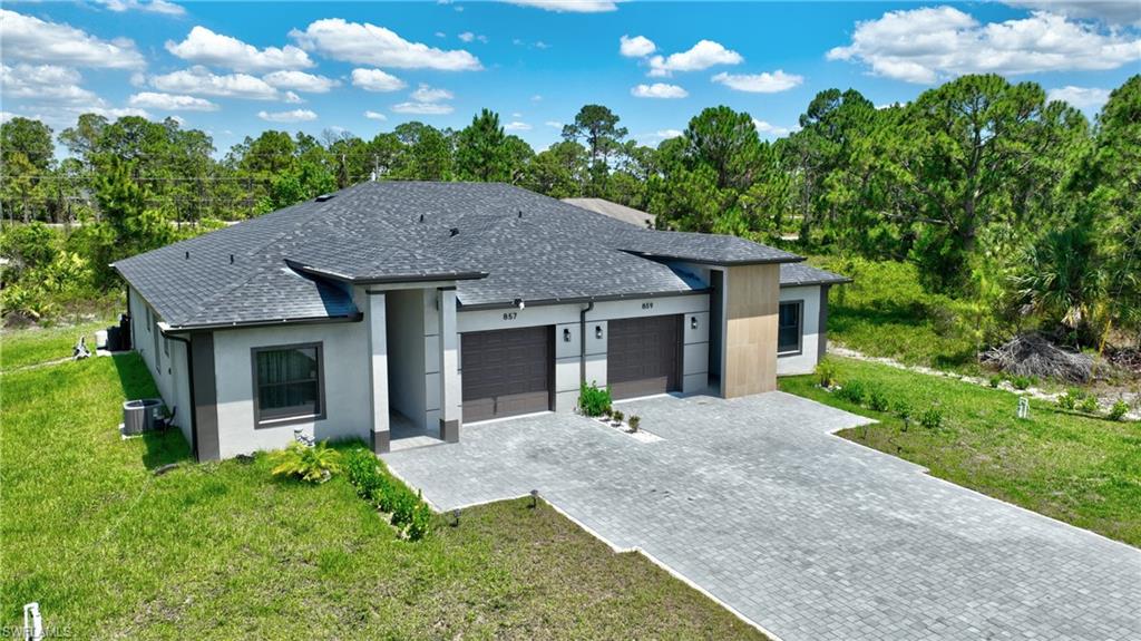 View of front of property featuring a shingled roof, a garage, decorative driveway, and a front lawn