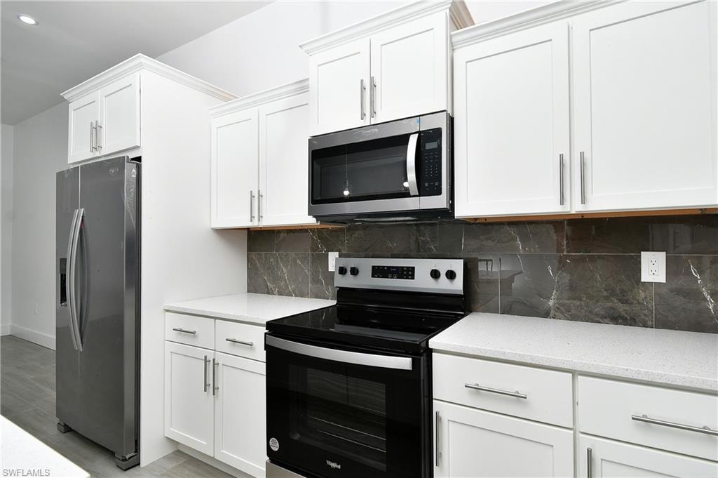 Kitchen featuring stainless steel appliances, white cabinets, light stone countertops, backsplash, and light wood-style flooring