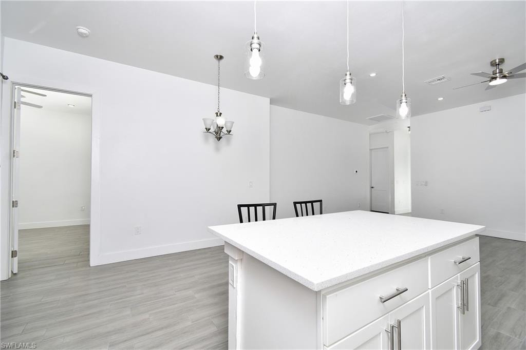Kitchen with ceiling fan, white cabinets, and pendant lighting