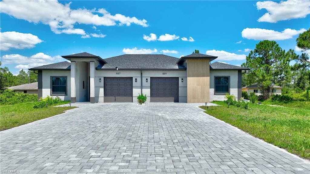 Prairie-style house with stucco siding, a front lawn, a garage, and decorative driveway