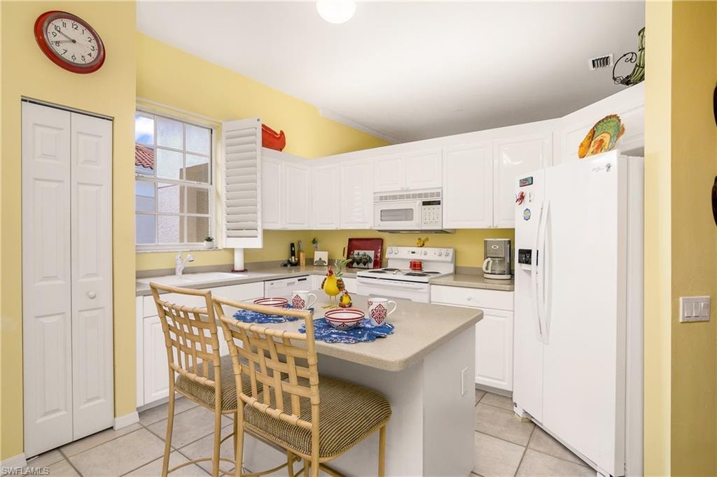 Kitchen with a center island, white appliances, white cabinets, light tile patterned floors, and a breakfast bar area