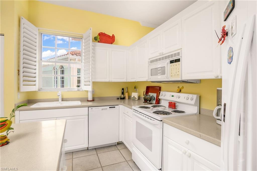 Kitchen with light tile patterned floors, white appliances, white cabinetry, and sink