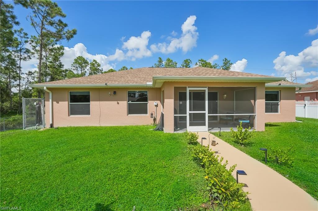 Rear view of property with stucco siding, a sunroom, roof with shingles, and a gate