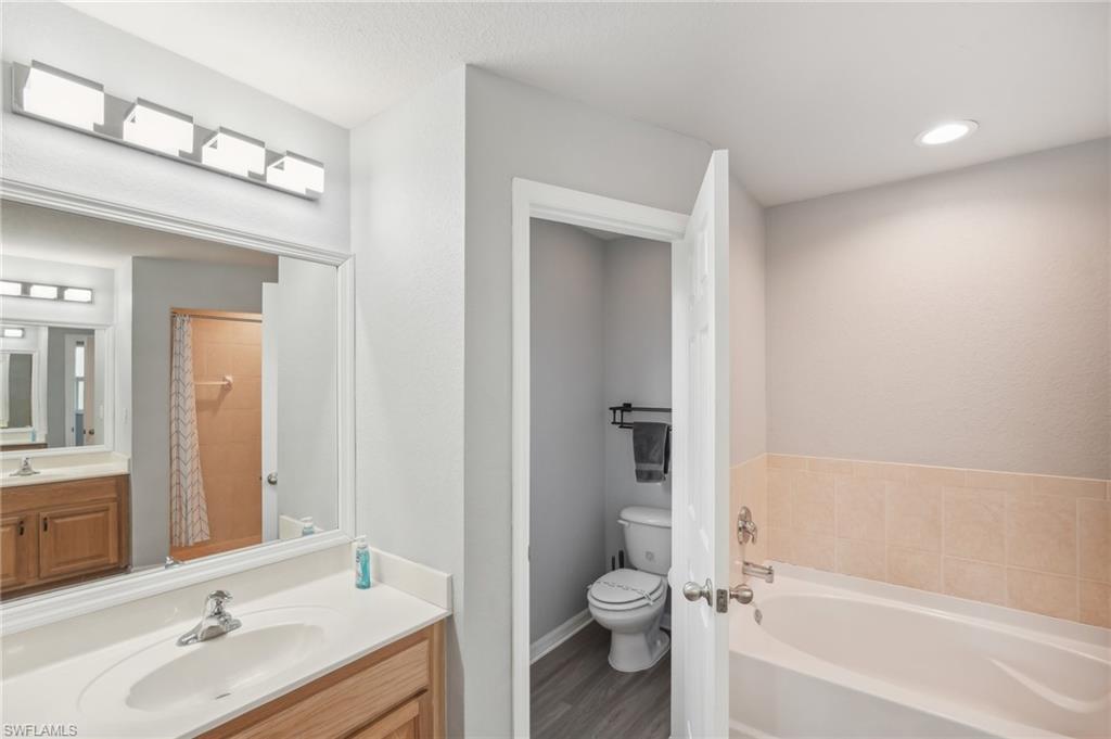 Full bath featuring a garden tub, vanity, a shower with shower curtain, and wood finished floors