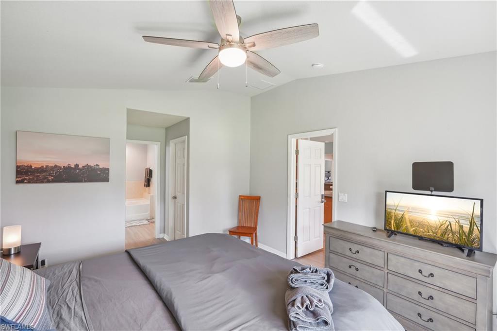 Bedroom with vaulted ceiling, a ceiling fan, ensuite bath, and light wood-style floors
