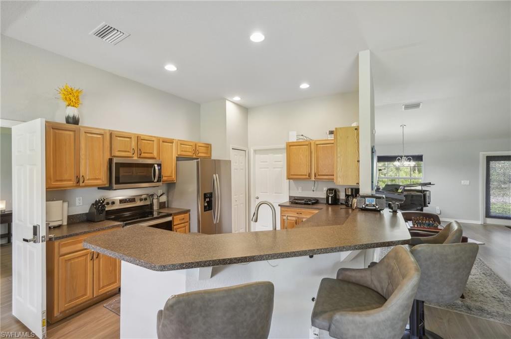 Kitchen featuring light wood finished floors, dark countertops, a peninsula, stainless steel appliances, and a kitchen bar