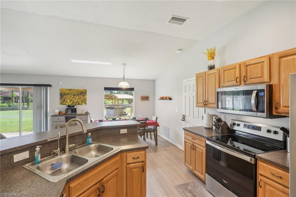 Kitchen featuring stainless steel appliances, dark countertops, lofted ceiling, decorative light fixtures, and light wood-style floors