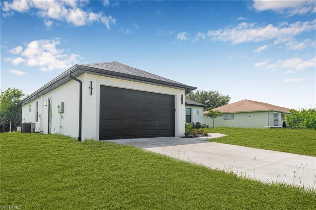View of side of home with a yard, driveway, stucco siding, and a shingled roof