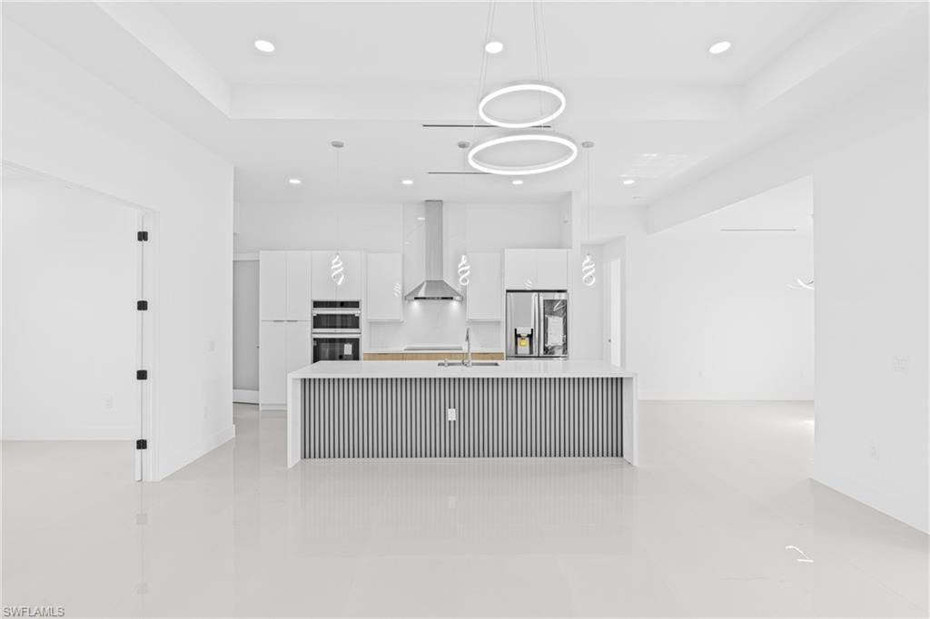Kitchen featuring modern cabinets, white cabinets, an island with sink, stainless steel appliances, and pendant lighting