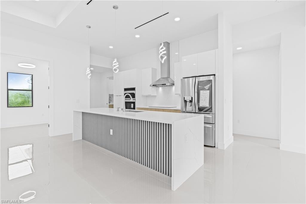 Kitchen with modern cabinets, white cabinetry, stainless steel fridge, decorative light fixtures, and an island with sink
