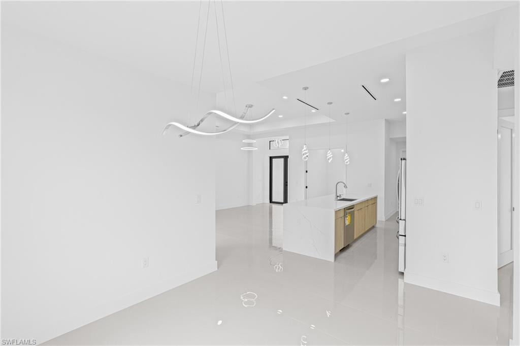 Kitchen with pendant lighting, light stone countertops, a center island with sink, stainless steel appliances, and modern cabinets