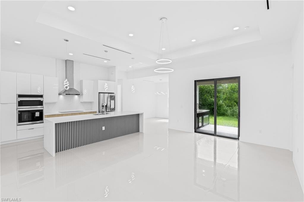 Kitchen featuring a center island with sink, decorative light fixtures, white cabinets, modern cabinets, and stainless steel appliances