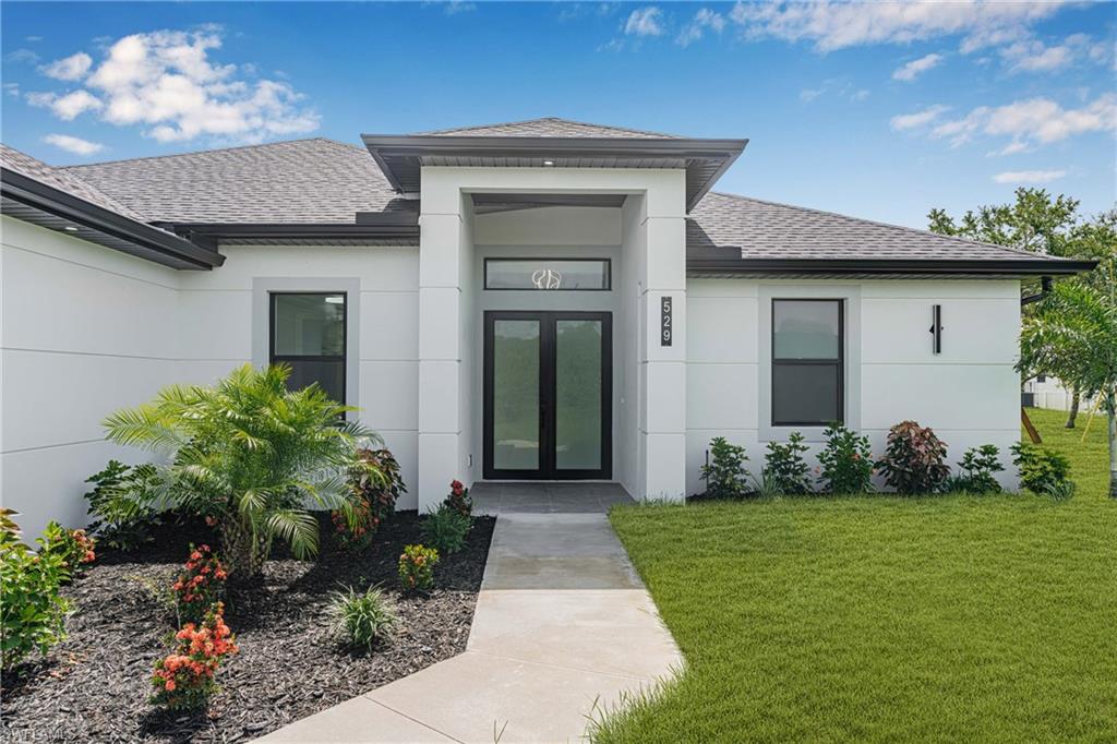 Doorway to property featuring a shingled roof, a yard, and stucco siding