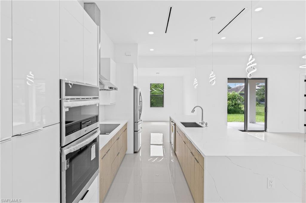Dual tone kitchen with modern cabinets, stainless steel appliances, light stone counters, hanging light fixtures, and two tone cabinets