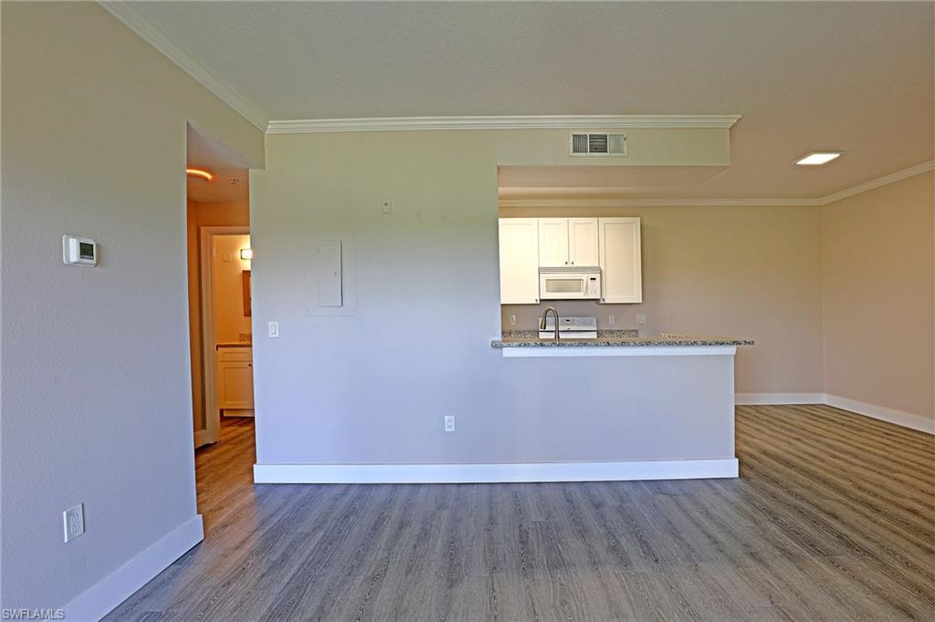 Kitchen featuring white cabinetry, dark stone counters, ornamental molding, white appliances, and wood finished floors