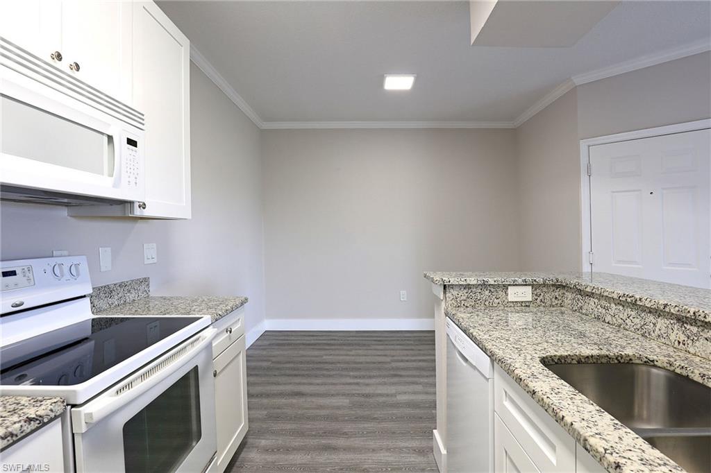 Kitchen featuring white appliances, white cabinets, light stone counters, dark wood finished floors, and crown molding