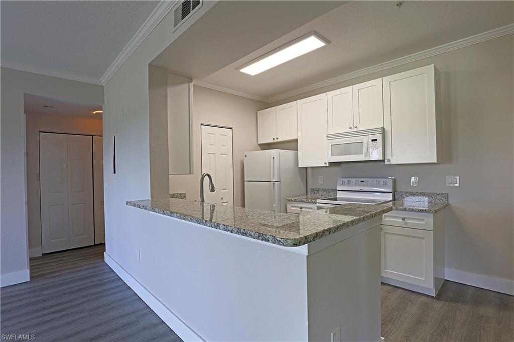 Kitchen featuring crown molding, white cabinets, dark stone countertops, white appliances, and a peninsula
