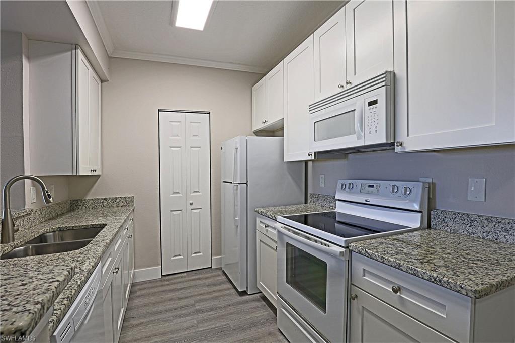 Kitchen with white appliances, white cabinets, crown molding, light stone counters, and dark wood finished floors