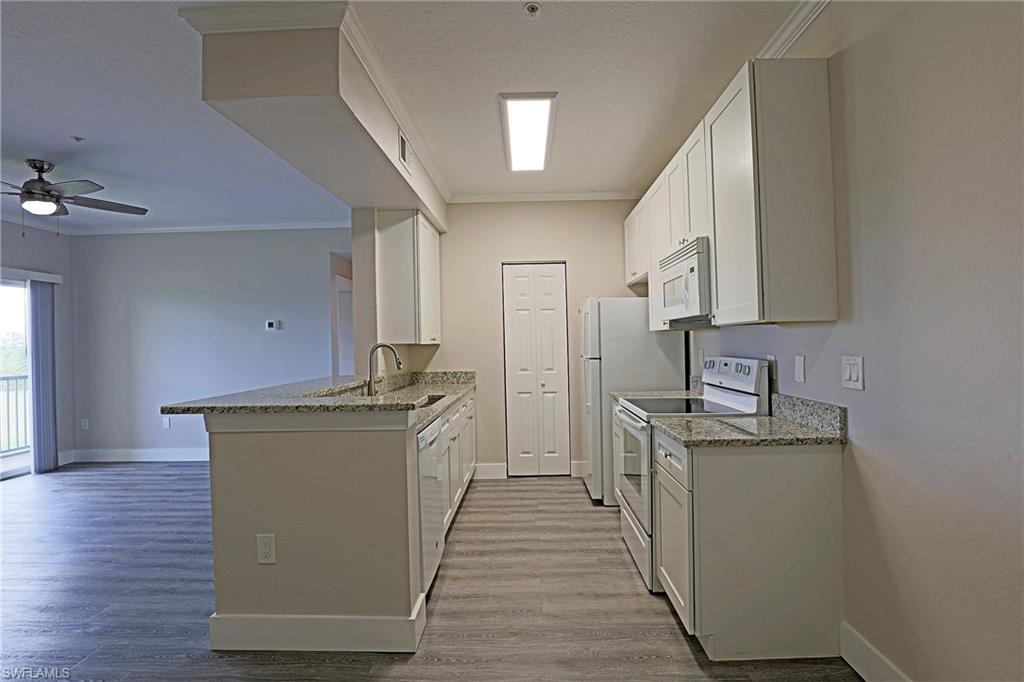 Kitchen featuring white appliances, white cabinetry, light stone counters, ornamental molding, and light wood finished floors