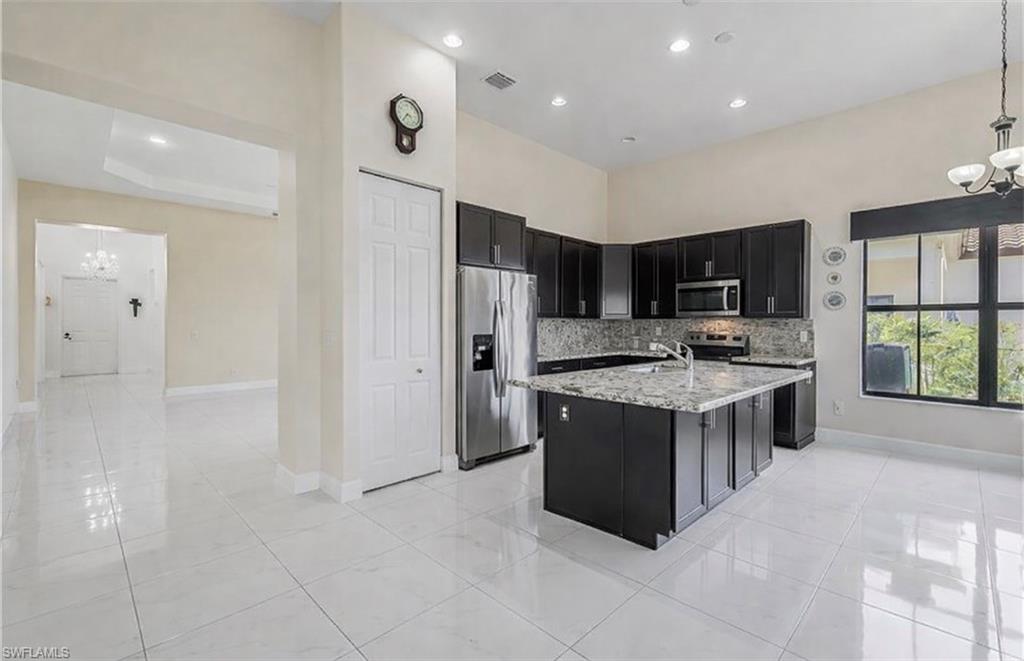 Kitchen featuring hanging lights, dark cabinetry, stainless steel appliances, and light stone countertops