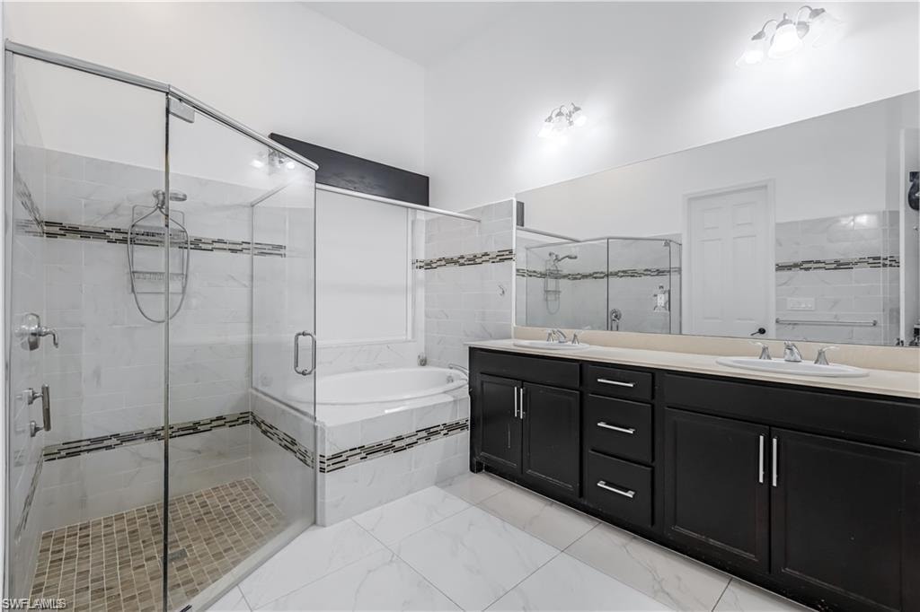 Full bathroom with a bath, a stall shower, double vanity, and light marble finish floors