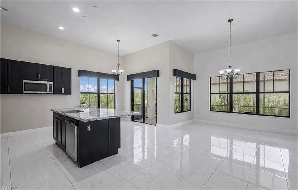 Kitchen featuring dark cabinets, suspended lighting, light stone countertops, and a high ceiling