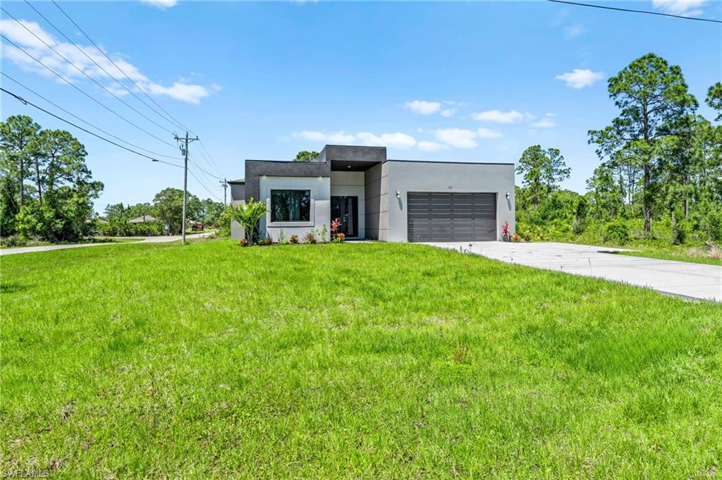Contemporary house featuring stucco siding, driveway, a front lawn, and a garage