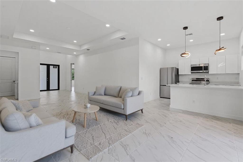 Living room with recessed lighting, light marble finish floors, a raised ceiling, and french doors