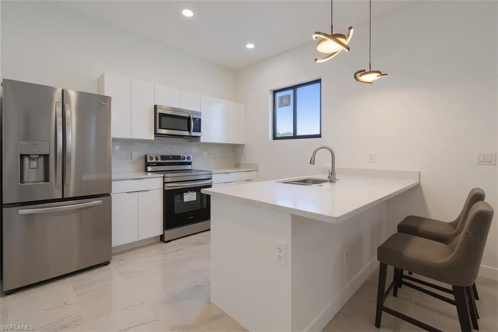 Kitchen with stainless steel appliances, a peninsula, a kitchen breakfast bar, white cabinets, and pendant lighting