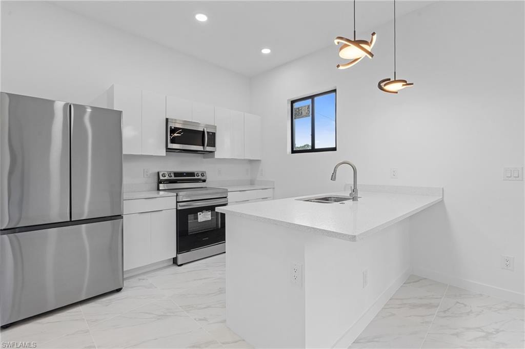 Kitchen with stainless steel appliances, light marble finish flooring, a peninsula, decorative light fixtures, and white cabinetry