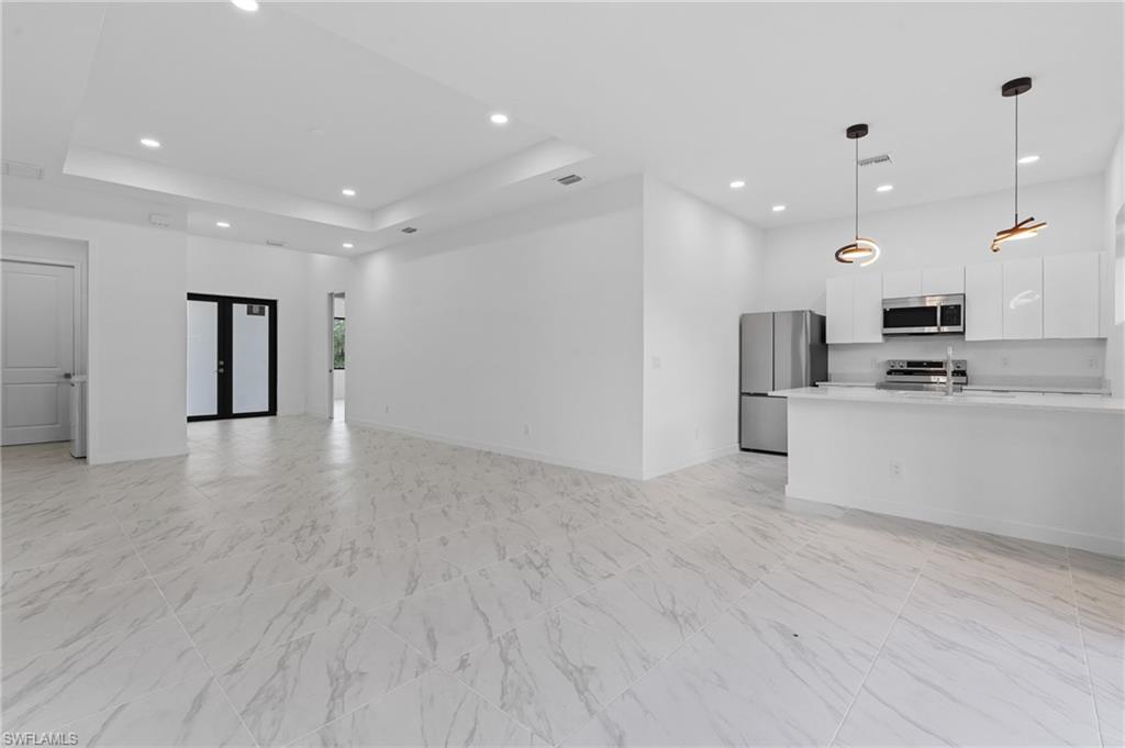 Unfurnished living room with recessed lighting, french doors, light marble finish floors, and a raised ceiling