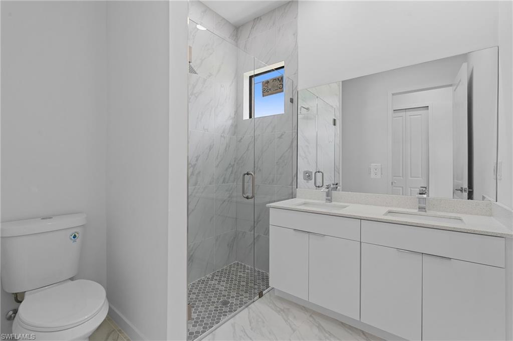 Full bath featuring a marble finish shower, double vanity, and light marble finish floors