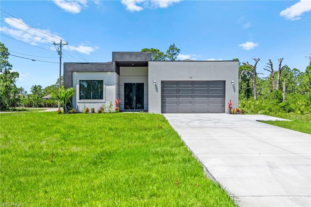 Contemporary house featuring a front yard, stucco siding, driveway, and a garage