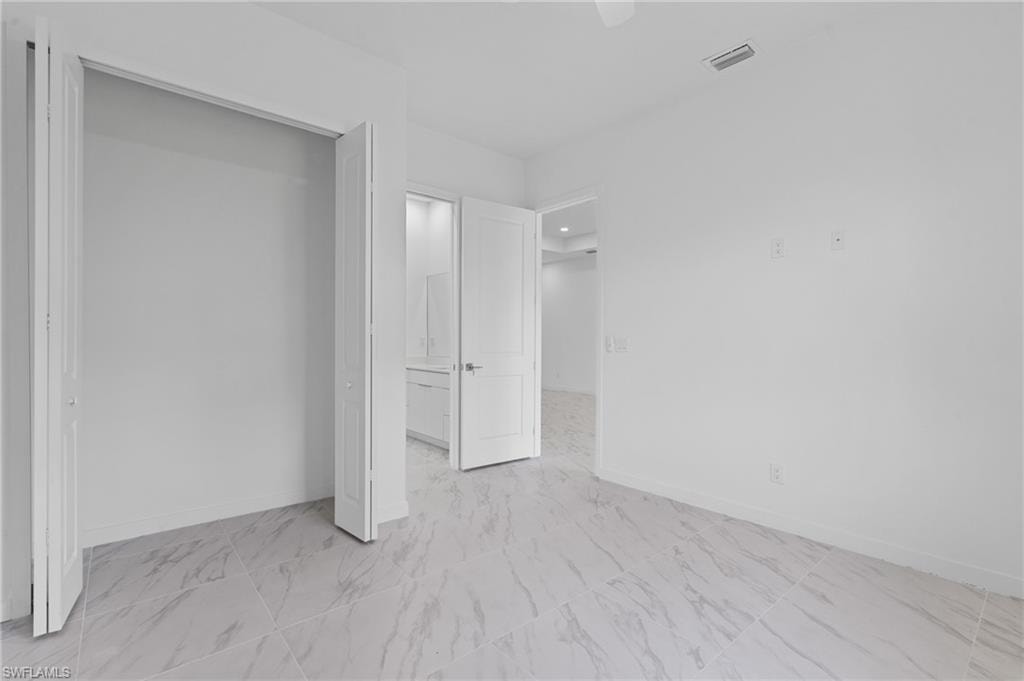 Unfurnished bedroom with ceiling fan, light marble finish flooring, ensuite bathroom, and a closet