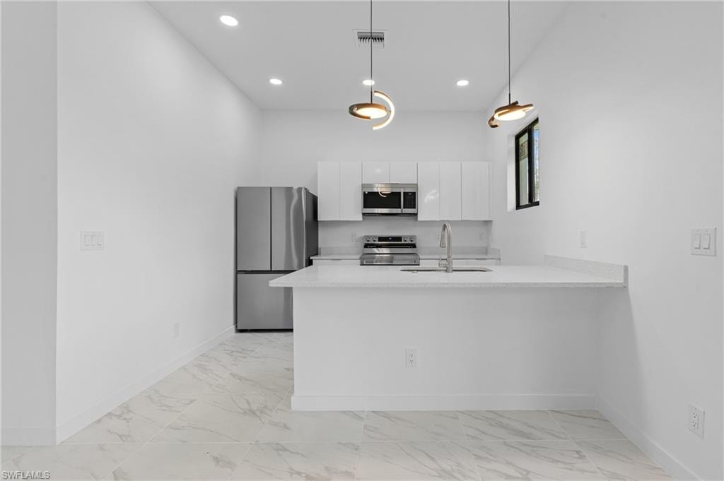 Kitchen with stainless steel appliances, a peninsula, white cabinets, hanging light fixtures, and light marble finish floors