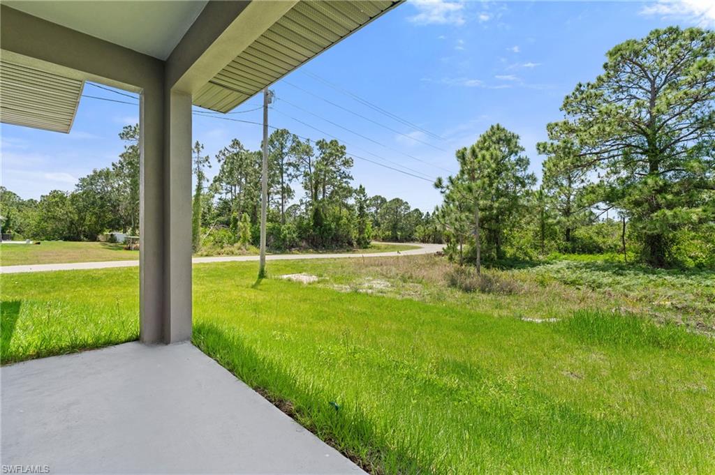 View of green lawn featuring view of wooded area and a porch