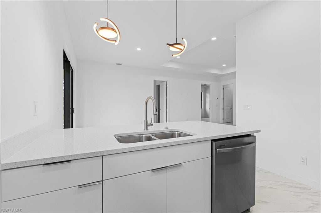 Kitchen with white cabinetry, stainless steel dishwasher, pendant lighting, light stone counters, and light marble finish flooring