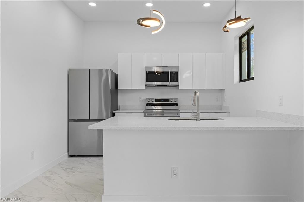 Kitchen with stainless steel appliances, a peninsula, light stone counters, modern cabinets, and white cabinets
