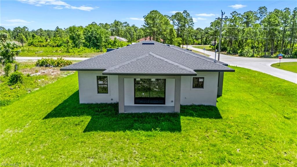 Back of house with stucco siding, a yard, and a shingled roof