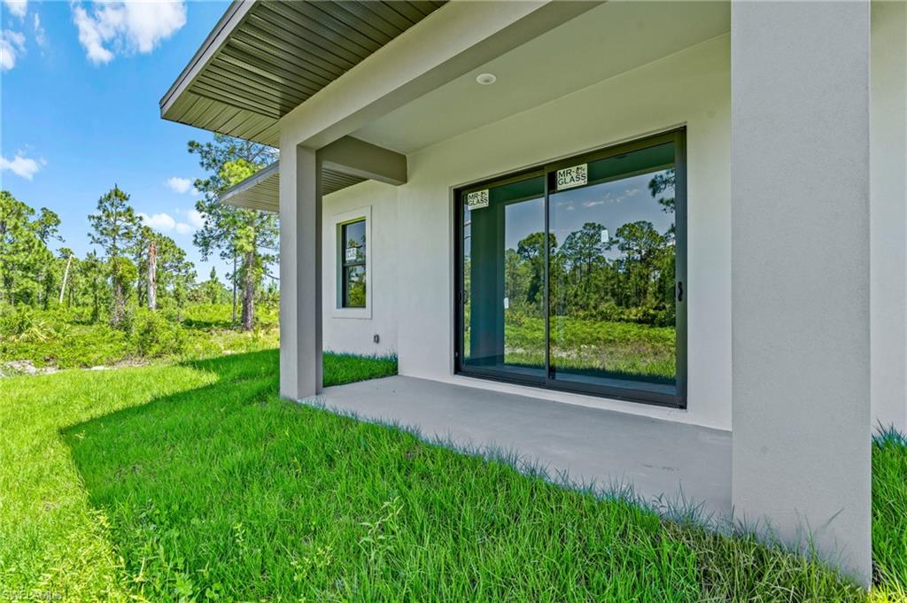 View of exterior entry with a patio, stucco siding, and a lawn