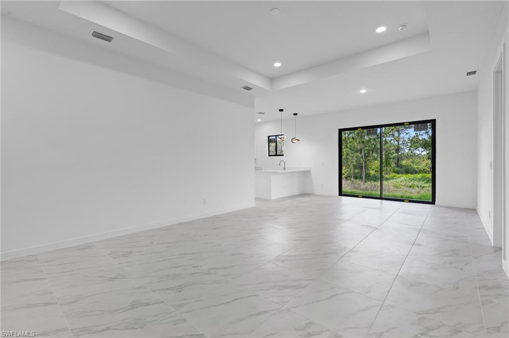 Unfurnished living room featuring a tray ceiling, light marble finish floors, and recessed lighting