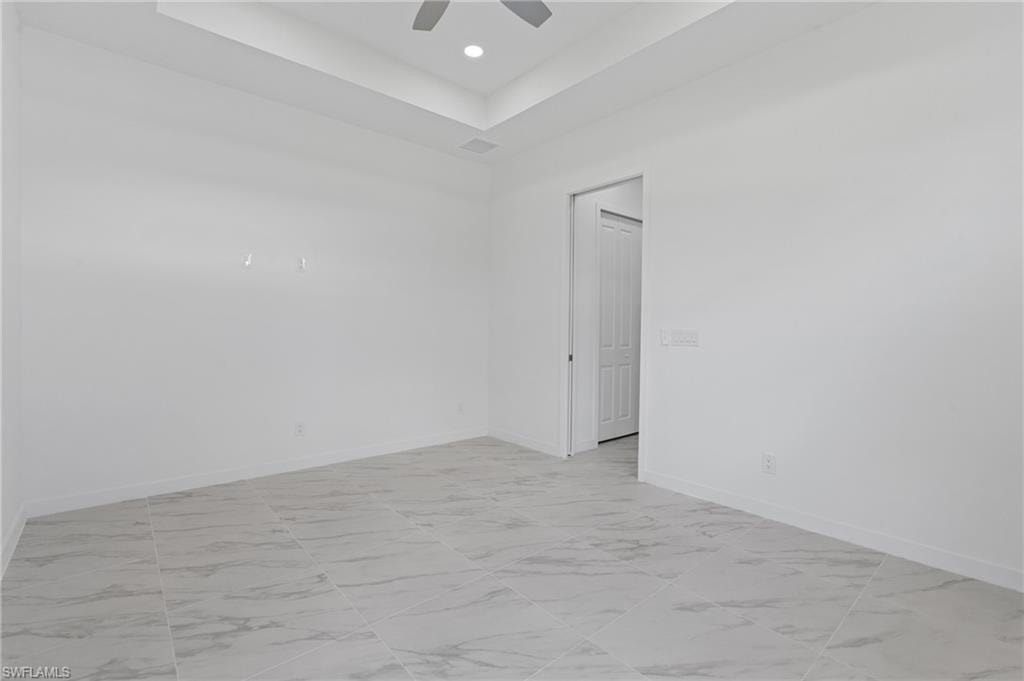 Empty room with a tray ceiling, light marble finish flooring, and recessed lighting