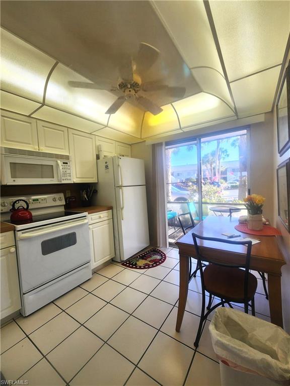 Kitchen with white appliances, white cabinets, a ceiling fan, dark countertops, and light tile patterned floors
