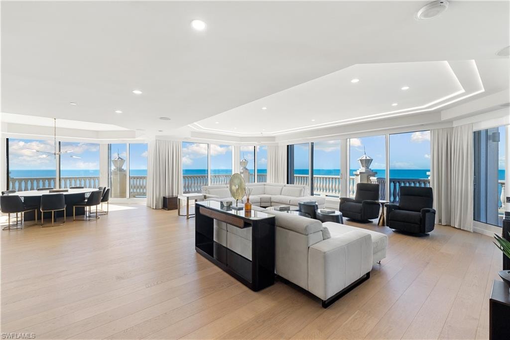 Living area featuring expansive windows, a tray ceiling, a water view, light wood-style flooring, and recessed lighting