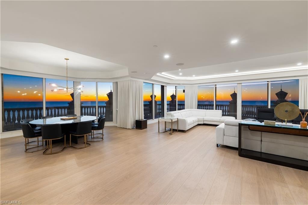 Living room featuring a raised ceiling, a water view, light wood-type flooring, and a chandelier