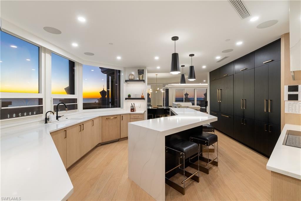 Two tone kitchen featuring a breakfast bar, a kitchen island, light wood-style flooring, light stone counters, and two tone cabinetry