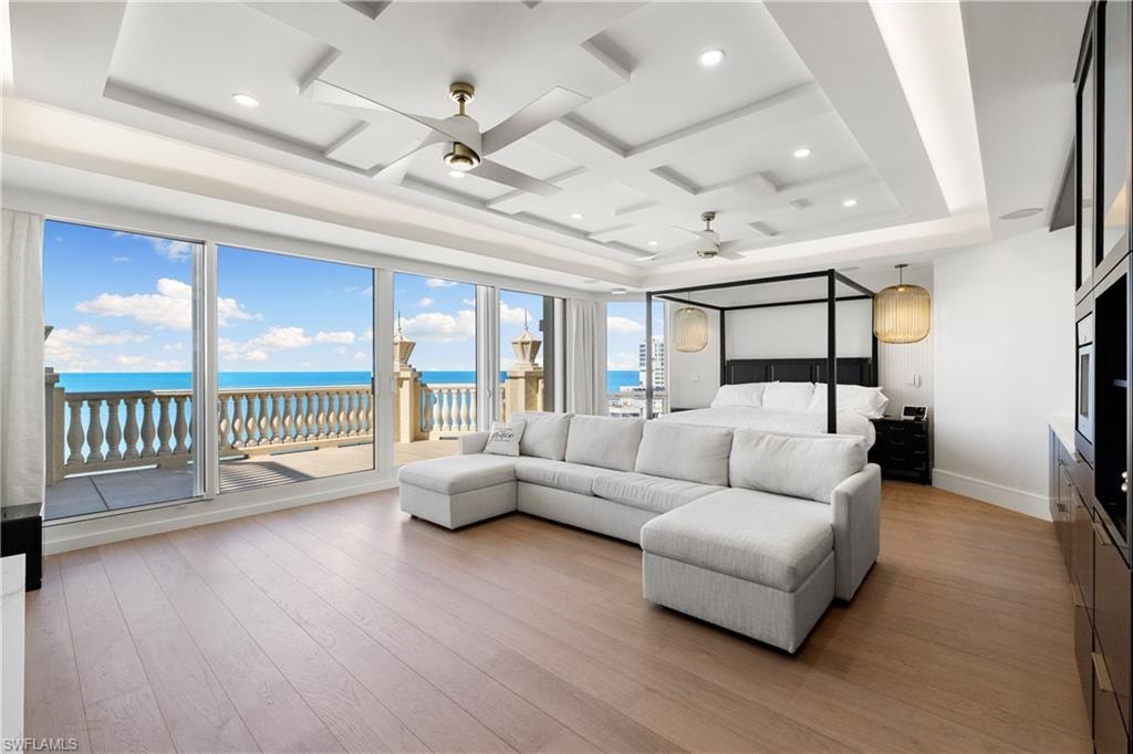Bedroom with a water view, access to outside, coffered ceiling, floor to ceiling windows, and light wood-style flooring