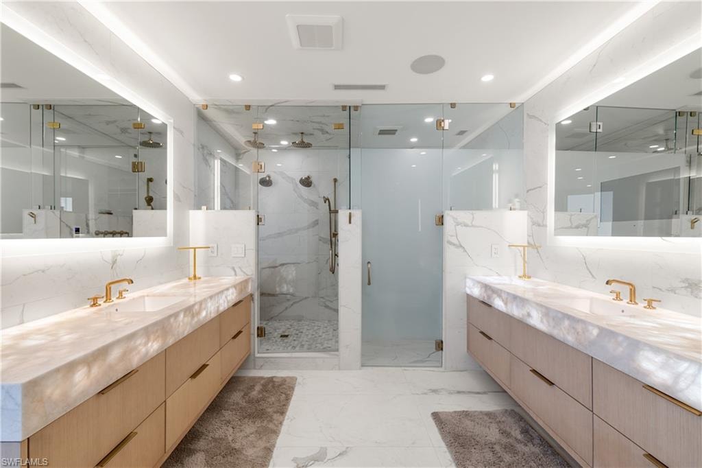 Full bath featuring two vanities, a marble finish shower, light marble finish flooring, and recessed lighting